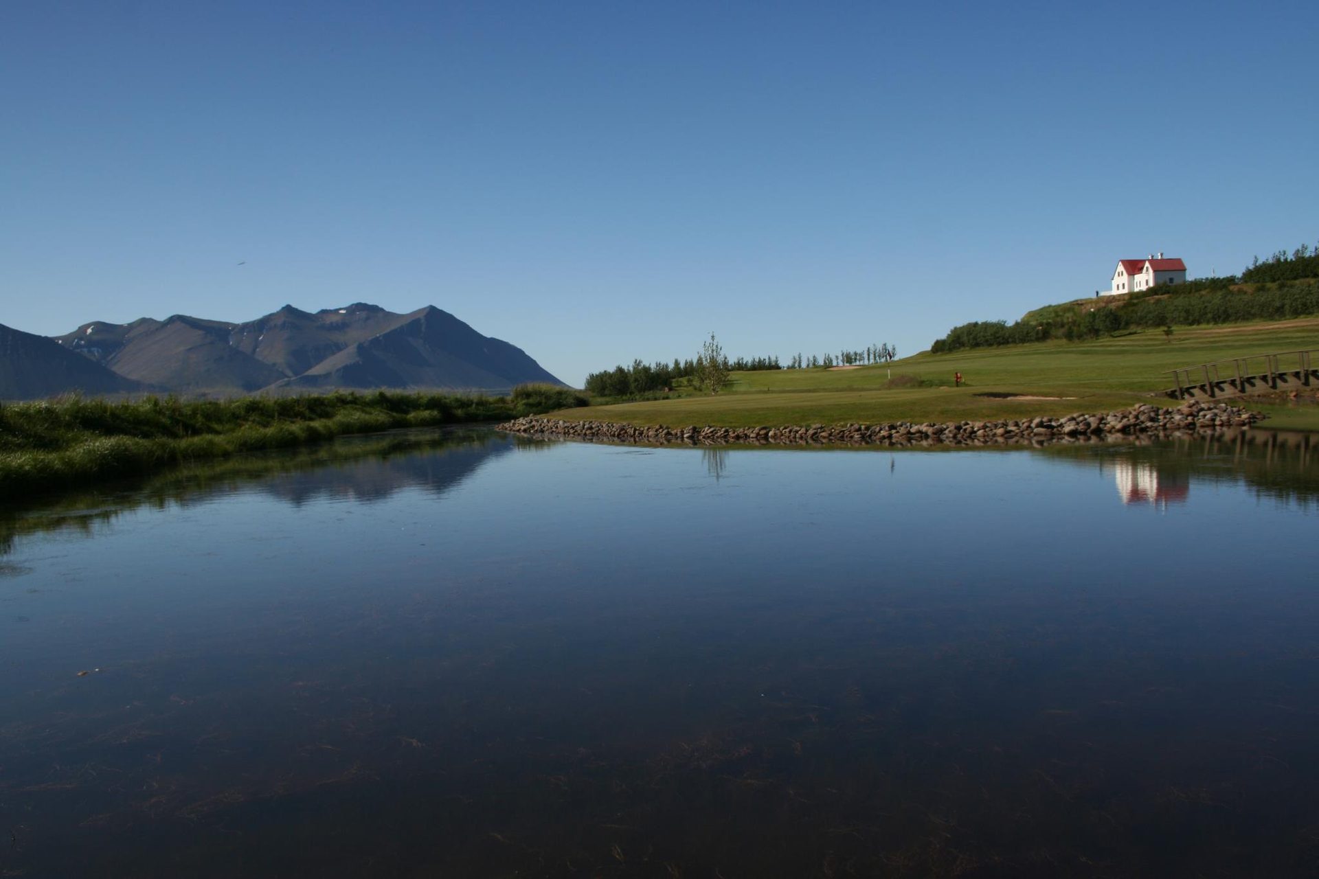 Golfvöllur við vatn með fjallasýn